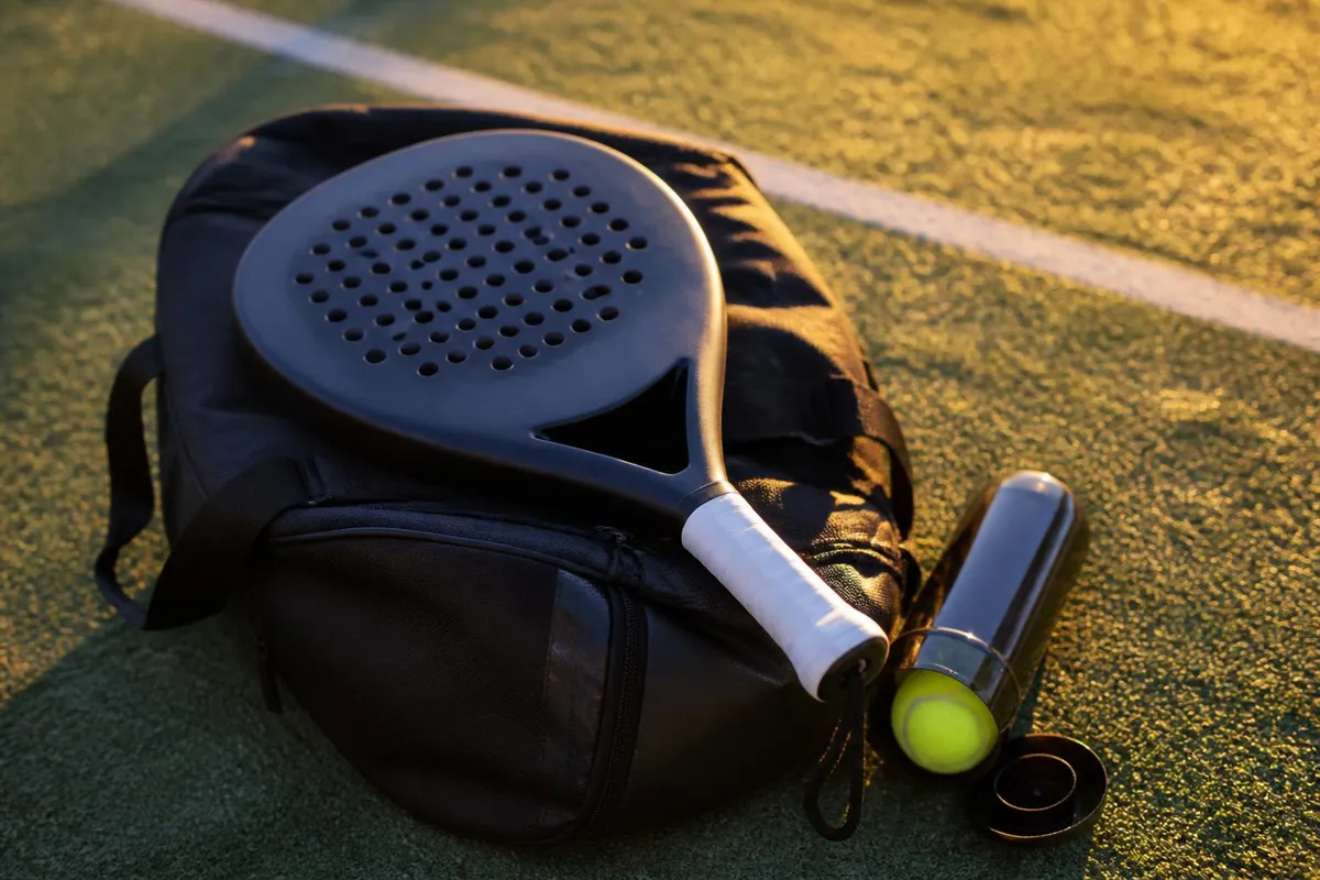 Une raquette de padel posée sur un sac de sport, à côté d'un tube de balles