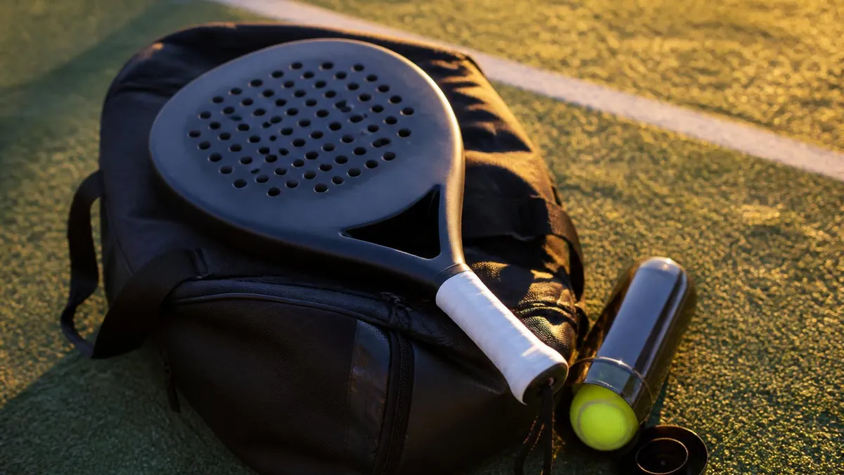 Une raquette de padel posée sur un sac de sport, à côté d'un tube de balles